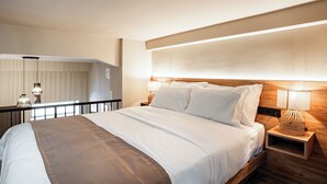 Hotellihuone, jossa on sänky, yöpöytälamput, puinen sängynpääty ja yöpöytä, jossa on lamppu.