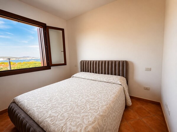 A bedroom with a bed, a window with a view, and a wall-mounted light switch.