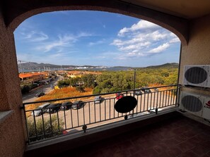 A balcony with a view of a coastal town, a parking area, and air conditioning units.