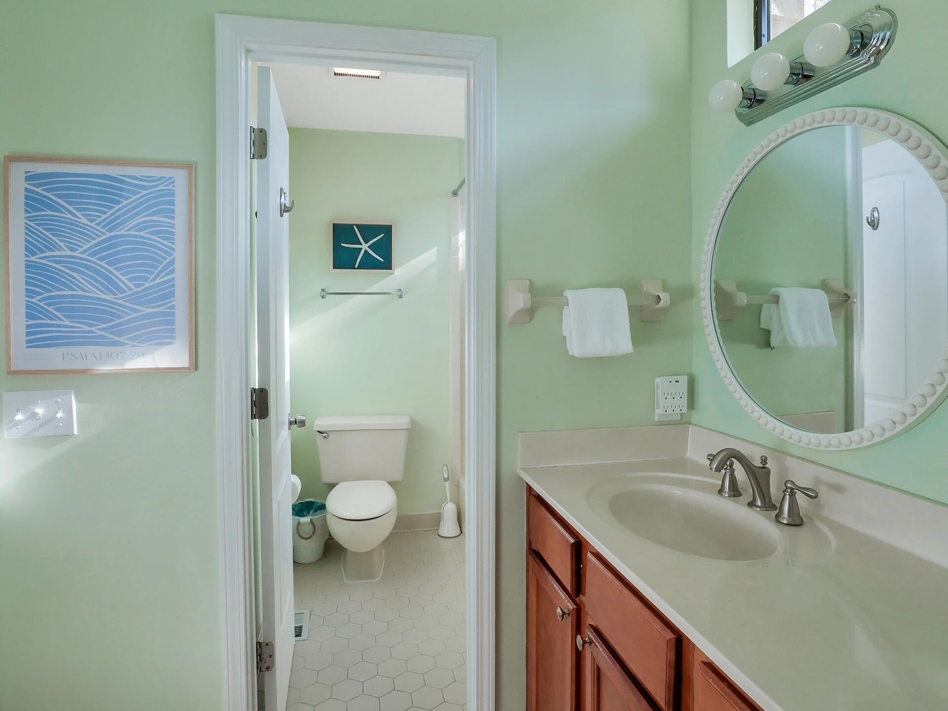 A bathroom with a toilet, sink, mirror, and a framed artwork on the wall.