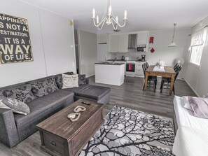 Una sala de estar moderna con sofá, mesa de centro y alfombra estampada. Se ve una cocina con comedor al fondo.