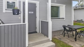 Una casita de una planta, con fachada gris, una puerta principal, una ventana y un patio con mesa y sillas.