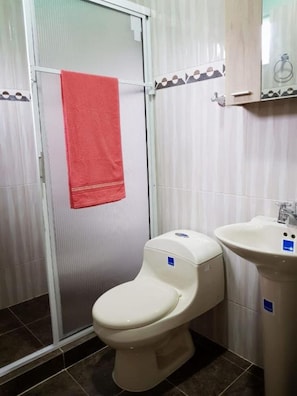 Ein Badezimmer mit Toilette, Waschbecken, einer Dusche mit Glastür und einem roten Handtuch, das an der Tür hängt.