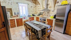 Uma cozinha com paredes de pedra, uma mesa de jantar, armários de madeira e uma geladeira de aço inoxidável.