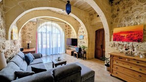 Uma sala de estar com parede de pedra, um sofá, uma TV, um armário de madeira e um quadro.