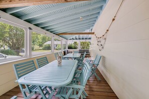 A covered outdoor seating area with tables and chairs, a view of the outdoors, and a wooden ceiling structure. - Incredible Screened Porch - Stay with Seaside Vacations! (Chincoteague Island)