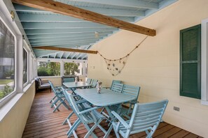 A covered patio with a table and chairs, wooden beams, and a view of greenery. - Incredible Screened Porch - Stay with Seaside Vacations! (Chincoteague Island)