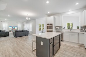 A modern kitchen with white cabinetry, a central island, and a dining area with a grey sofa. - Great Amenities + Dog Friendly! (Greenbackville)