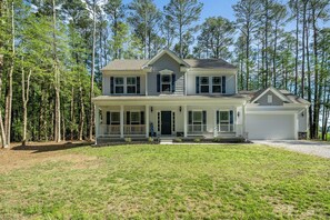 A two-story house with a front porch, garage, and a wooded backdrop. - Great Amenities + Dog Friendly! (Greenbackville)