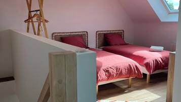 Une chambre avec un plafond en pente, un puits de lumière, un lit avec une literie rouge, une échelle en bois et un luminaire suspendu.