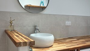 Un bagno moderno con uno specchio rotondo, un lavandino bianco e un piano d'appoggio in legno.