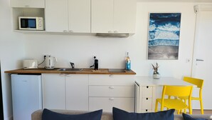 A compact kitchen with a microwave, toaster, and sink. There is a small table with a chair, a refrigerator, and a painting on the wall. - Houseboat Aveiro 3 (Aveiro)