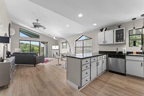 A modern kitchen with a central island, built-in cabinets, and a dining area with a sofa and a TV. - Green Mountain Getaway 2bdr (Branson)