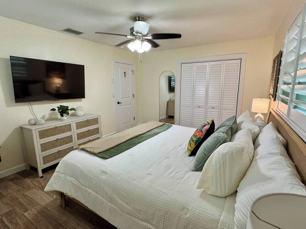 Une chambre à coucher comprenant un lit, une commode, un téléviseur, un ventilateur de plafond et un placard.
