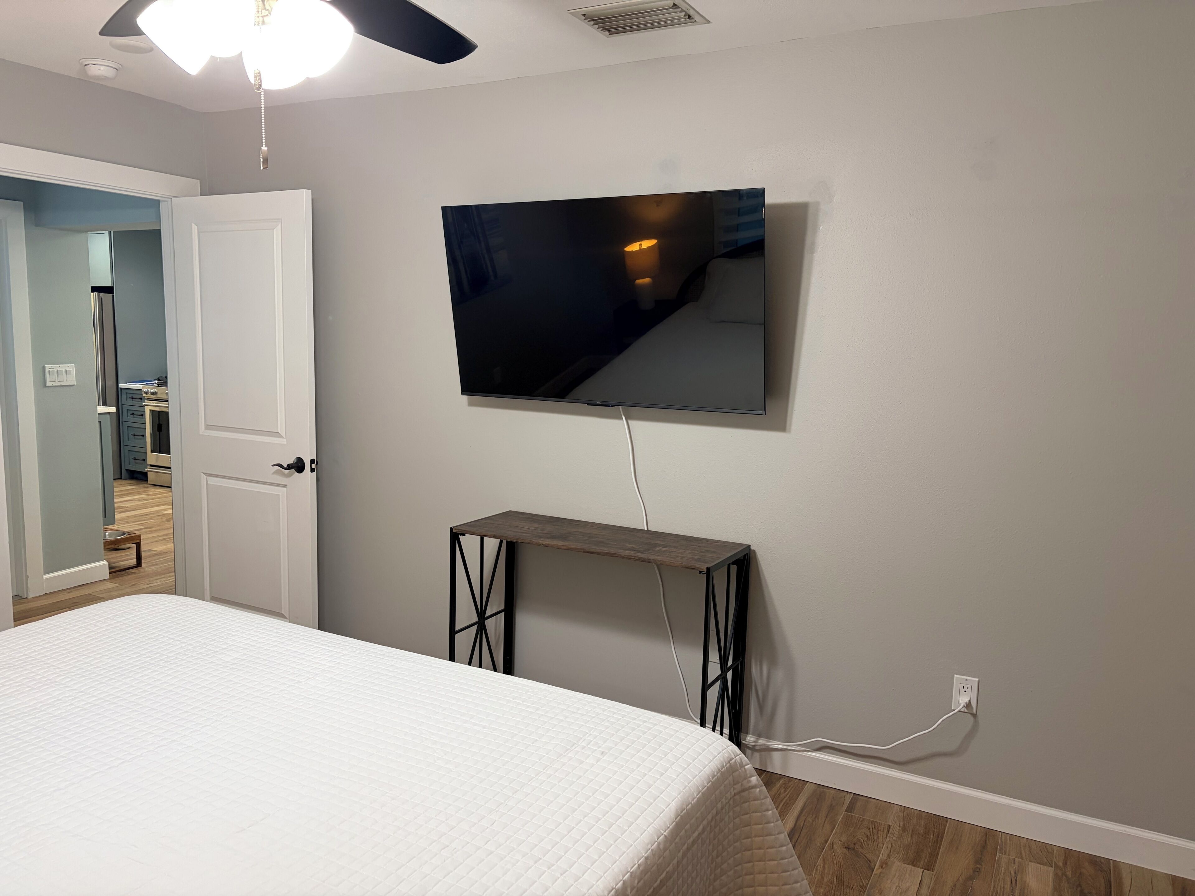 Een slaapkamer met een bed, een aan de muur bevestigde televisie, een plafondventilator en een deur naar een andere kamer.
