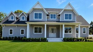 A two-story house with a front porch, a well-maintained lawn, and a clear blue sky. - New Construction 6-bed walk to Westhampton Beach train station for US Open (Westhampton Beach)