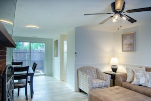 Un salon doté d’un ventilateur de plafond, d’un canapé, d’un fauteuil à motifs, d’une petite table avec une lampe, et d’un coin repas avec des chaises et une table.
