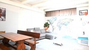 Ein Wohnzimmer mit einem Holzesstisch, einem grauen Sofa und einer Weltkarte an der Wand.