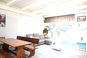 A living room with a wooden dining table, grey sofa, and a world map on the wall. - P100 - Porto Recanati, new centrally located two-room apartment with parking space (Porto Recanati)