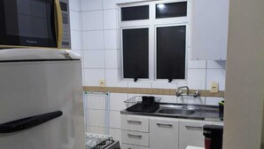 Una cocina con armarios blancos, estufa a gas, microondas y ventana sobre el lavamanos.