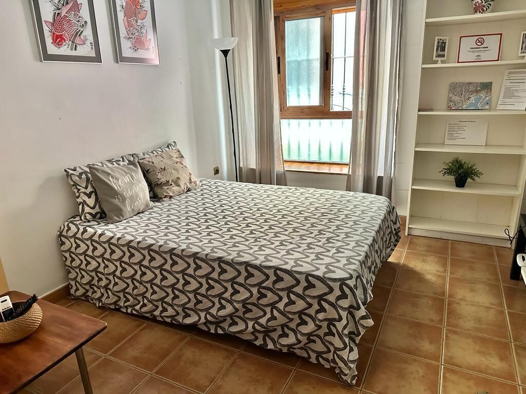 Een slaapkamer met een bed met een decoratieve spreideken, een nachtkastje met een mand, en een raam met gordijnen.