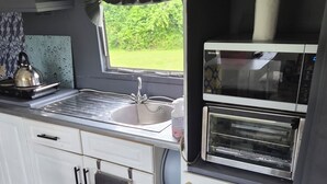 A compact kitchen with a sink, kettle, and oven. - EXCLUSIVE MOBILE HOME
BASED IN COUNTRYSIDE BUT CLOSE TO AIRPORT AND TOWNS (Aldergrove)