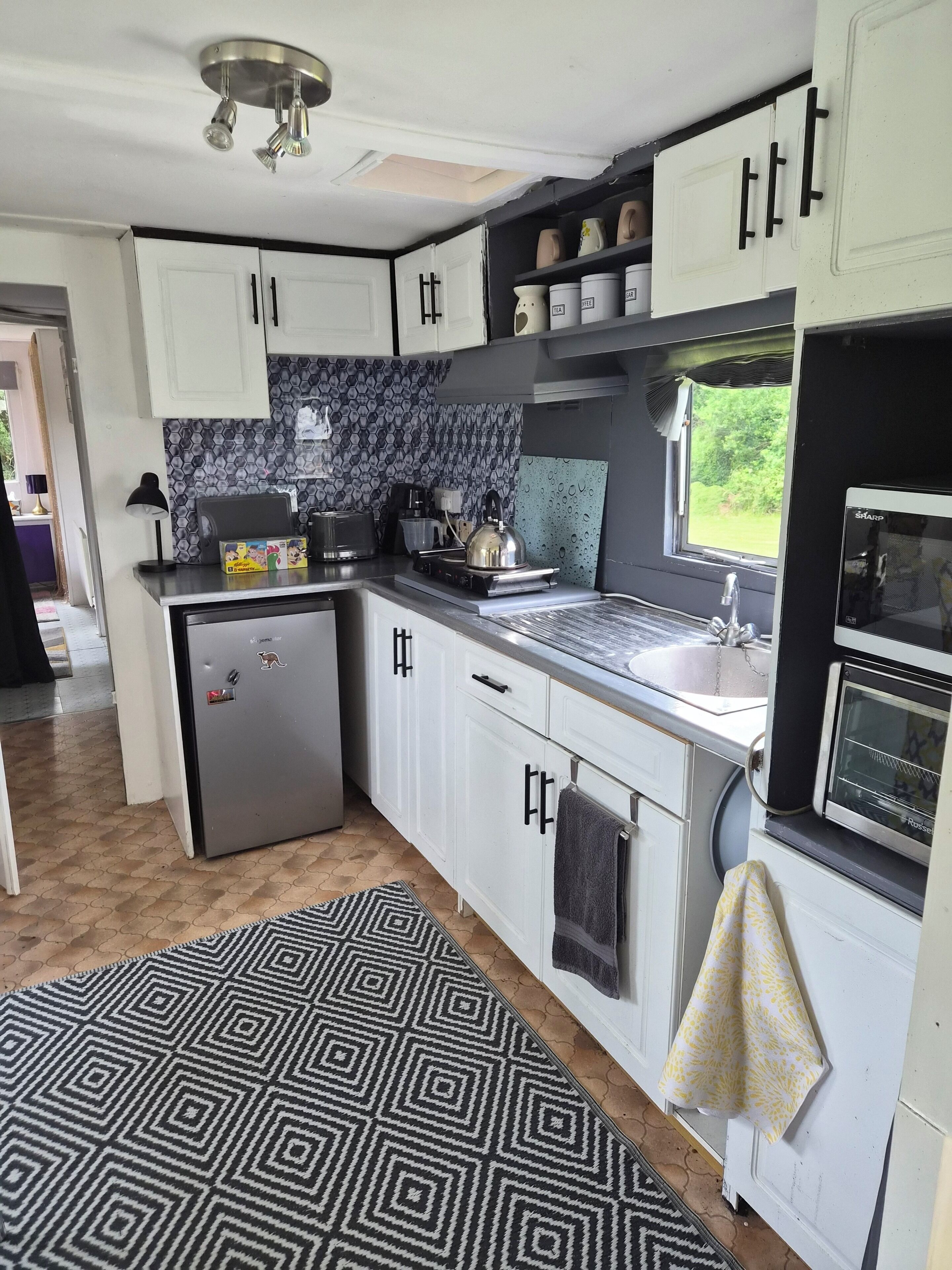 A compact kitchen with white cabinets, a built-in oven, a sink, and a patterned rug.