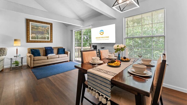 Una sala de estar moderna con comedor, un ventanal grande y un televisor mostrando 'GRAND WELCOME BRANSON & THE OZARKS'.