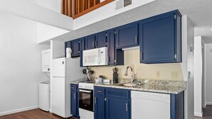 Una cocina moderna con electrodomésticos blancos, armarios azules y encimera de granito.