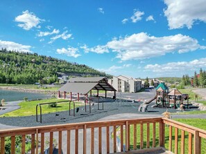 A playground with swings and a climbing structure, a covered picnic area, and a view of a lake and forested hills. - Giant Steps 45 Ski in/ Ski out (Brian Head)