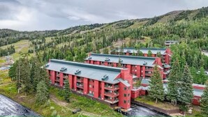 Ett rött hotell med flera våningar och balkonger, omgivet av ett skogbeklätt landskap.