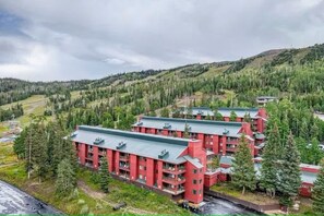 A multi-story building with a red facade and green roofs, surrounded by dense forest and hills. - Giant Steps 45 Ski in/ Ski out (Brian Head)