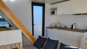 A compact living space with a kitchenette, a sofa with cushions, a wooden staircase, and a view through a door. - Houseboat Aveiro 4 (Aveiro)