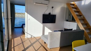 A modern room with a grey sofa, a yellow chair, a wooden staircase, and a TV mounted on the wall. - Houseboat Aveiro 4 (Aveiro)