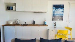 A compact kitchen with a microwave, toaster, and sink. There is a small table with a chair, a refrigerator, and a painting on the wall. - Houseboat Aveiro 4 (Aveiro)