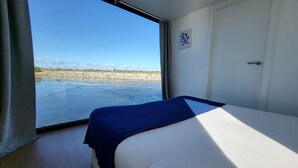 A room with a bed, a window with a view of a beach, and a door. - Houseboat Aveiro 4 (Aveiro)