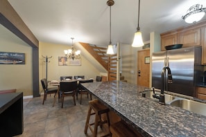 Eine Küche mit Granit-Arbeitsplatten, einem Edelstahl-Kühlschrank, Holzbarhocker und einem Essbereich mit Tisch und Stühlen.