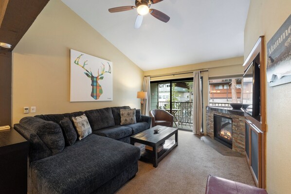 A living room with a sectional sofa, a coffee table, a fireplace, and a ceiling fan. - Comfortable Slope-Side Stroll Condo 658 (Mammoth Lakes)