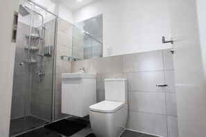 A modern bathroom with a glass-enclosed shower, a white toilet, and a sink. - Cozy 1-bedroom apartment in charming Accra with AC and gym (Accra)