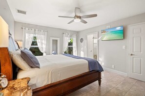 Ein Schlafzimmer mit einem Bett, einem Deckenventilator, einem Fernseher und einer Tür.