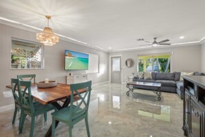 A spacious living room with a wooden dining table, green chairs, a sofa, a coffee table, and a television. - The Seahorse Hideaway (Lake Worth Beach)