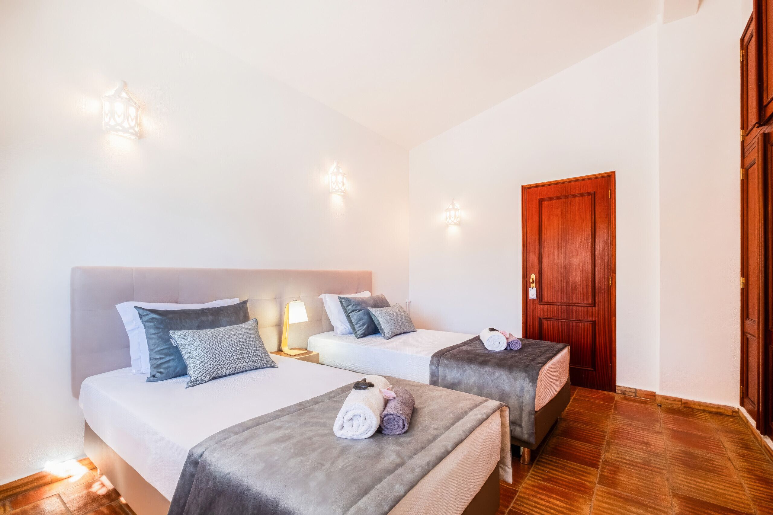 A hotel room with two beds, each with a headboard, bedside lamps, and towels.