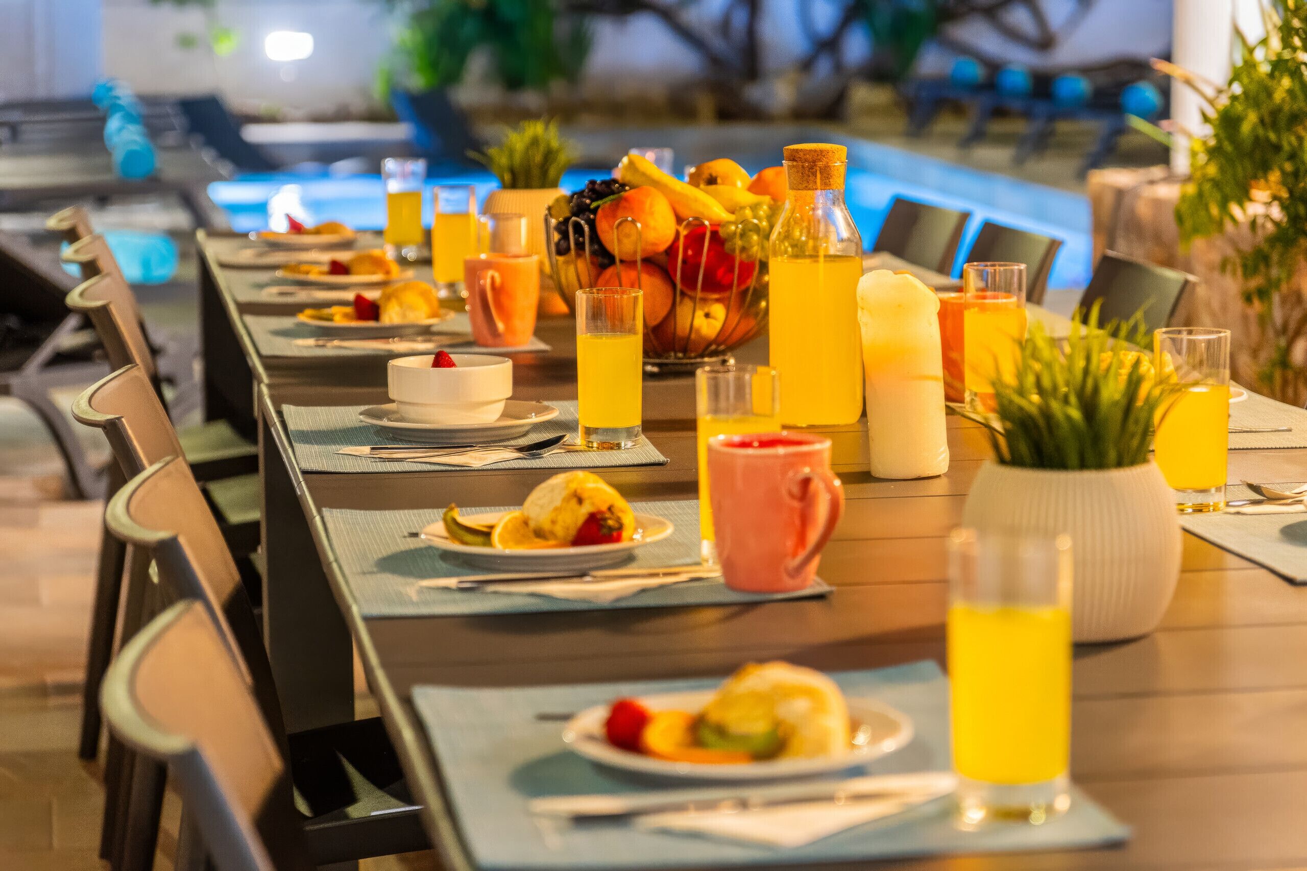 Mesa de comedor preparada con platos, cubiertos y diversas bebidas, como jugo y agua, en un ambiente de restaurante.