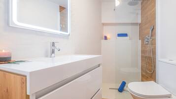 A modern bathroom with a white vanity, a mirror, a shower, and a toilet.