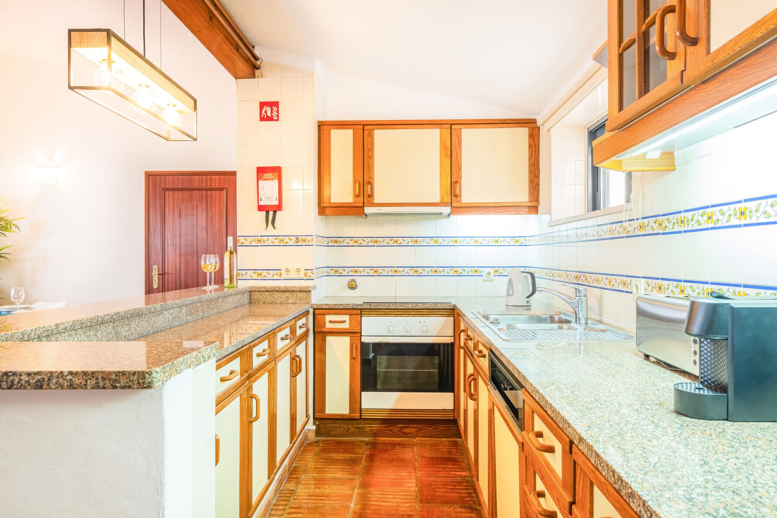 A kitchen with wooden cabinets, a built-in oven, a stainless steel sink, and a tiled backsplash.