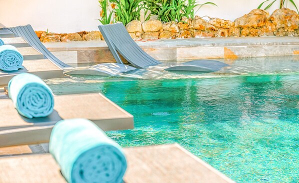 A pool area with lounge chairs and a stone border.