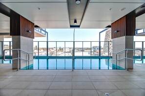 An indoor swimming pool with a view of the cityscape, metal railings, and a tiled floor. - Bright & Modern 2BR | Pool & Wellness Facilities (Adelaide)