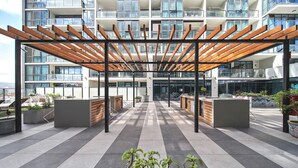 En moderne udendørs terrasse med et træbeklædt pergola, siddeområder og udsigt til en skyskraber.