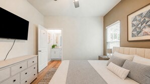 A bedroom with a bed, a TV, a ceiling fan, a nightstand, a window with blinds, and a painting on the wall. - The Brainerd House · 3BR, EV Charger, Private Yard (Pensacola)
