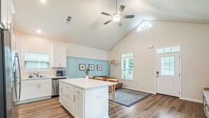 A kitchen with white cabinets, a central island, a ceiling fan, and a door with a window. - The Brainerd House · 3BR, EV Charger, Private Yard (Pensacola)
